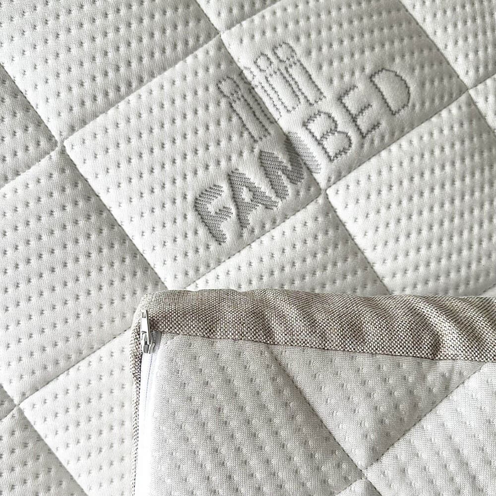 Närbild av bäddmadrassens quiltade vita överdrag med invävd FAMBED-logotyp