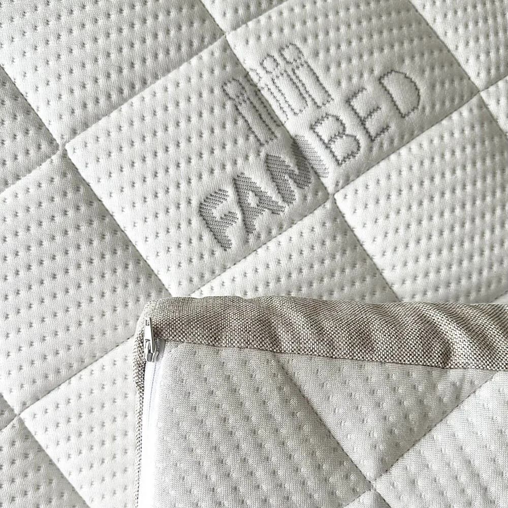 Närbild av bäddmadrassens quiltade vita överdrag med invävd FAMBED-logotyp