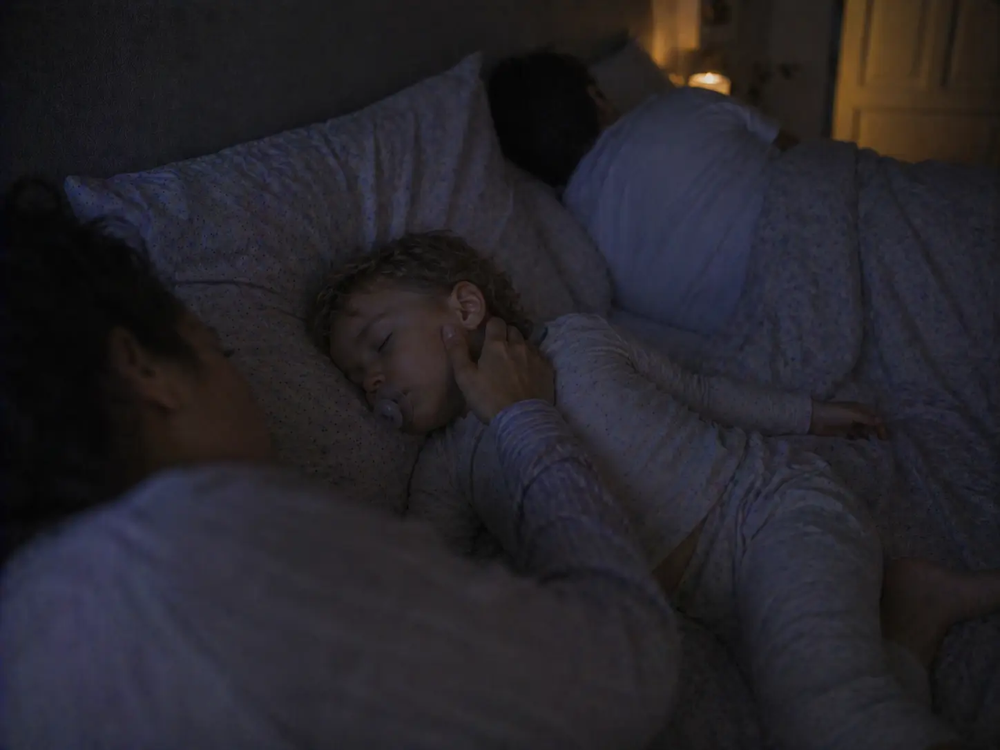 En mamma rör försiktigt vid sitt sovande barns kind i familjesängen på natten