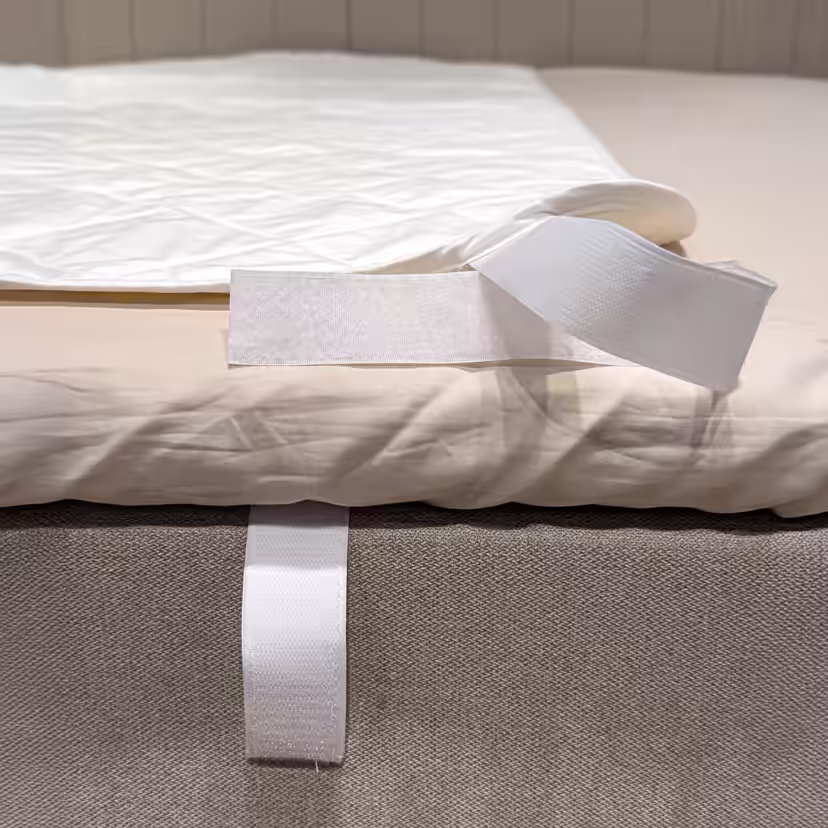 Hörnet på det vita, quiltade madrasskyddet är vikt tillbaka så att kardborrebandet runt sängkanten syns